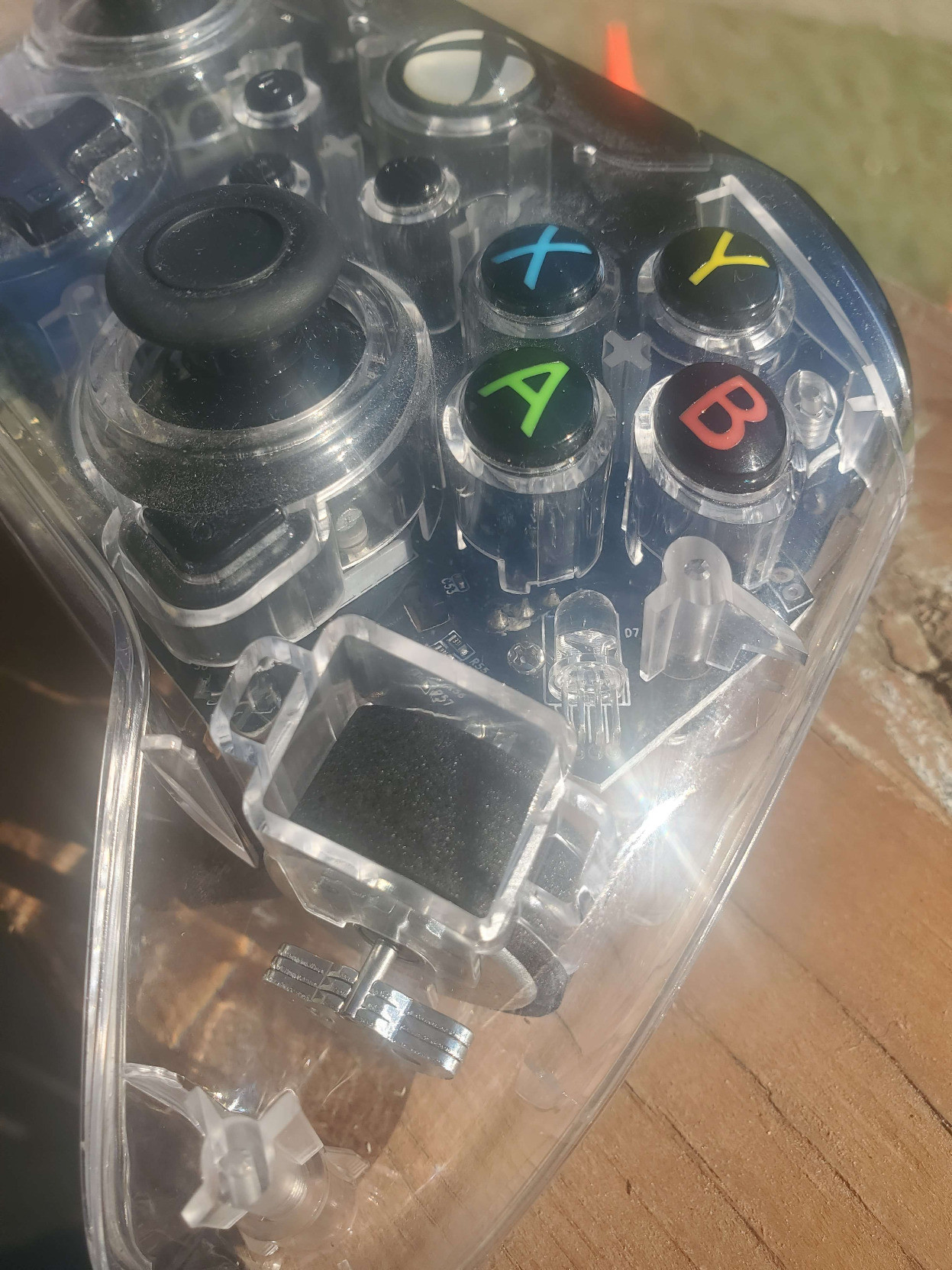 alt-text: pictures of a clear plastic xbox controller. It's shown on my porch-deck with the sunlight streaming in, and there seems to be a sparkle in the sheen of the transparent covering. Perhaps it's reflections from the various circuits and gizmos that are apparent in it's central form, or perhaps it's simply a trick of the light. Upon being placed in shadow, the inner-workings do not appear to sparkle in that same way, so perhaps the beauty is derived from the slivers of the sun that danced across the space between earth and our star. In any case, the entire controller is quite dusty, as if it had been hidden in a paper grocery bag that was shoved in the back of the closet of a boy who doesn't think to clean often. Frankly it's just not worth the trouble, and if he made any messes he would pick them up... but why bother with the little stuff? it's good enough, this is how he lives, so why would we be inconsiderate of his lifestyle? the final picture is of the audio jack.