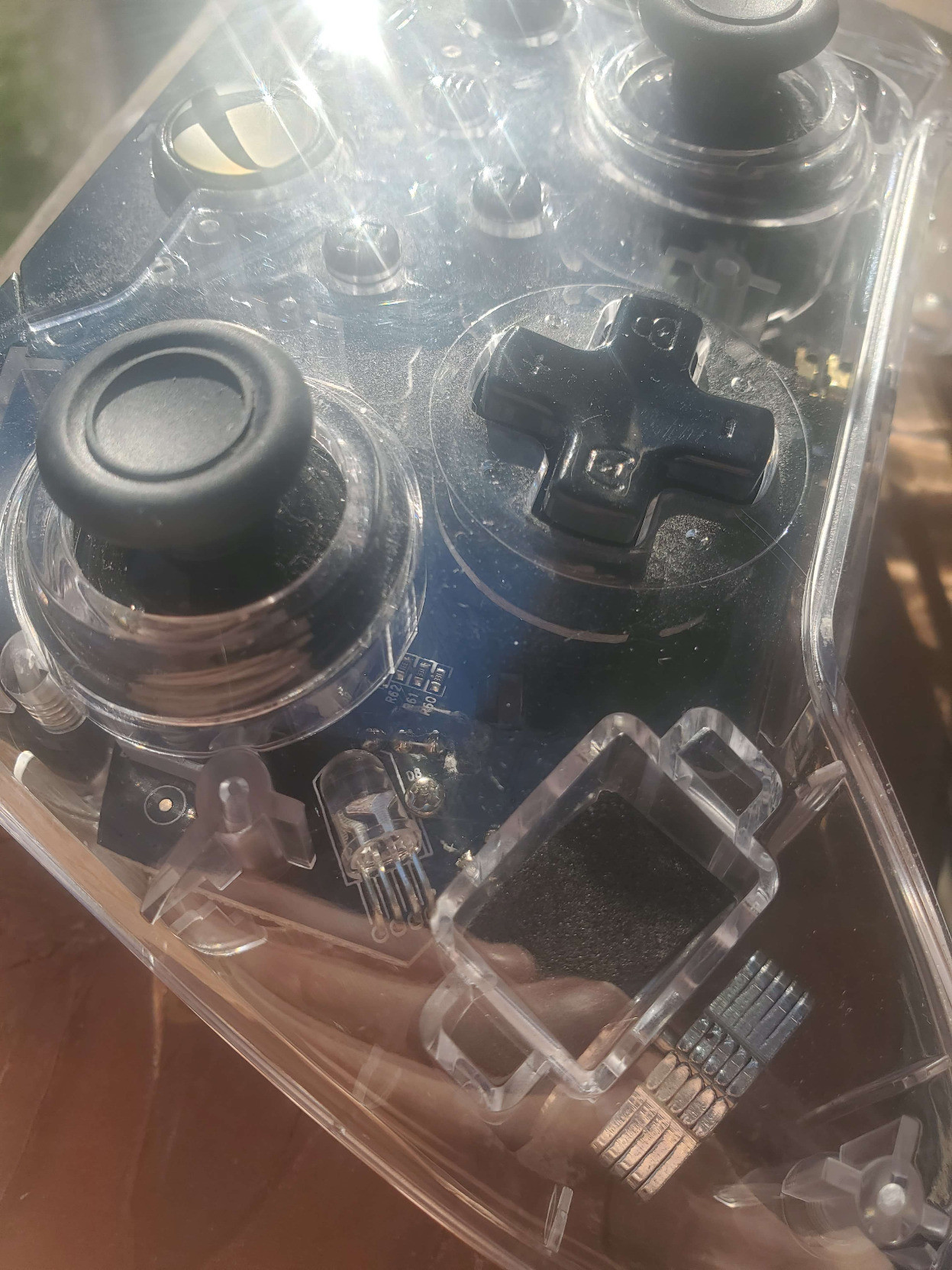 alt-text: pictures of a clear plastic xbox controller. It's shown on my porch-deck with the sunlight streaming in, and there seems to be a sparkle in the sheen of the transparent covering. Perhaps it's reflections from the various circuits and gizmos that are apparent in it's central form, or perhaps it's simply a trick of the light. Upon being placed in shadow, the inner-workings do not appear to sparkle in that same way, so perhaps the beauty is derived from the slivers of the sun that danced across the space between earth and our star. In any case, the entire controller is quite dusty, as if it had been hidden in a paper grocery bag that was shoved in the back of the closet of a boy who doesn't think to clean often. Frankly it's just not worth the trouble, and if he made any messes he would pick them up... but why bother with the little stuff? it's good enough, this is how he lives, so why would we be inconsiderate of his lifestyle? the final picture is of the audio jack.